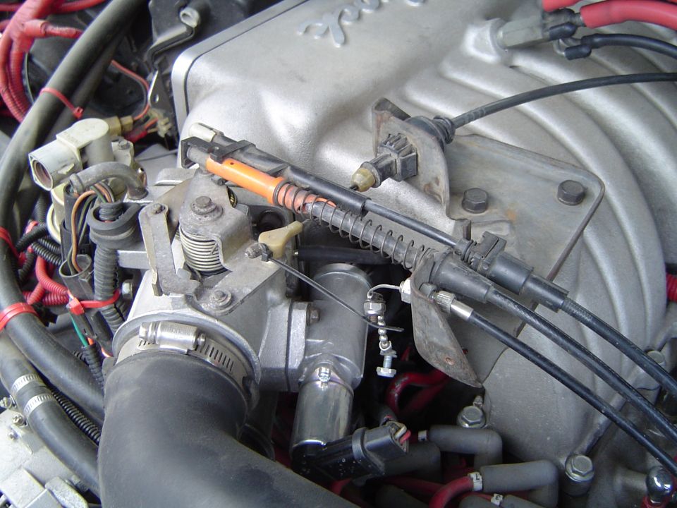 Engine bay close-up with throttle linkage, cables, and red plug wires