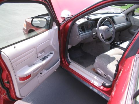 2001 Ford Crown Victoria - View of the interior of a red sedan, showing the dashboard, steering wheel, and front seats with the driver's door ajar.