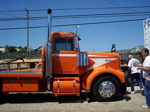 1981 Kenworth W900A - This orange Kenworth semi-truck features a flatbed trailer and a prominent chrome exhaust stack.