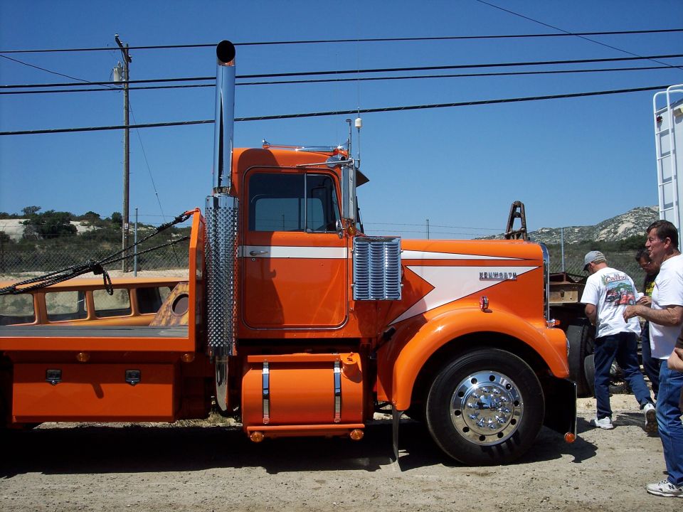 Orange Kenworth W900A flatbed truck side view with chrome stack and polished wheels
