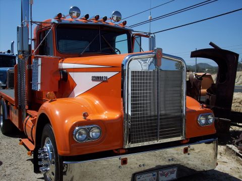 1981 Kenworth W900A - Front view of an orange Kenworth truck, a prominent chrome grille and distinctive white stripe on the fender.