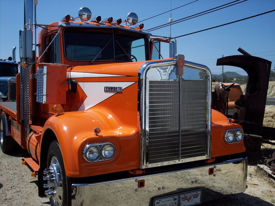 Orange Kenworth truck with chrome grille and white stripe on fender. California license plate visible