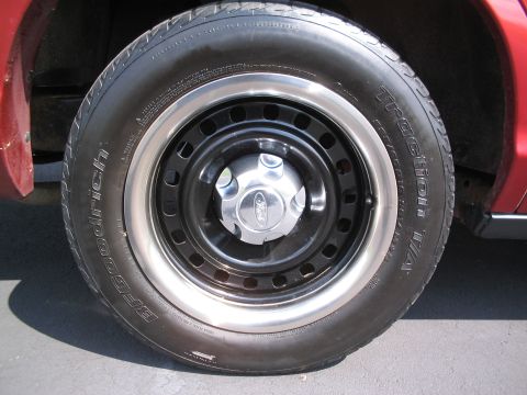 2001 Ford Crown Victoria - Close-up of a red vehicle's wheel and tire assembly, showing a Ford logo on the hubcap.