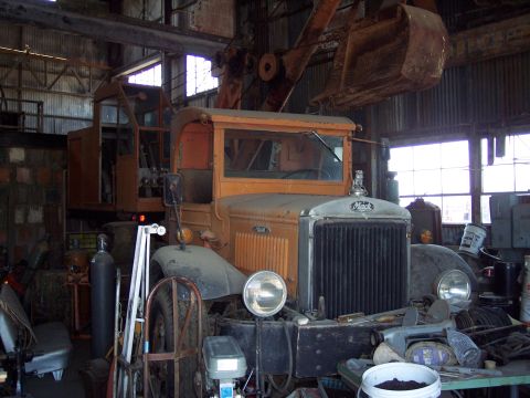 1981 Kenworth W900A - An orange Mack truck, equipped with a crane, sits inside a cluttered workshop.