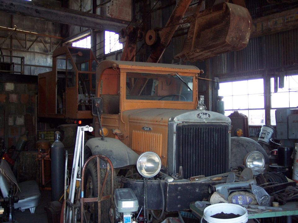 Orange Mack truck with crane attachment, front view, in a workshop