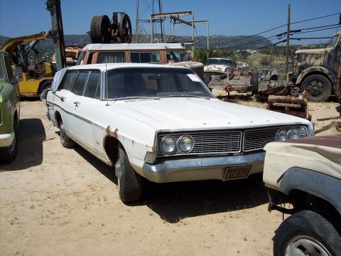 1981 Kenworth W900A - A white station wagon sits in a junkyard with other vehicles and scrap metal.