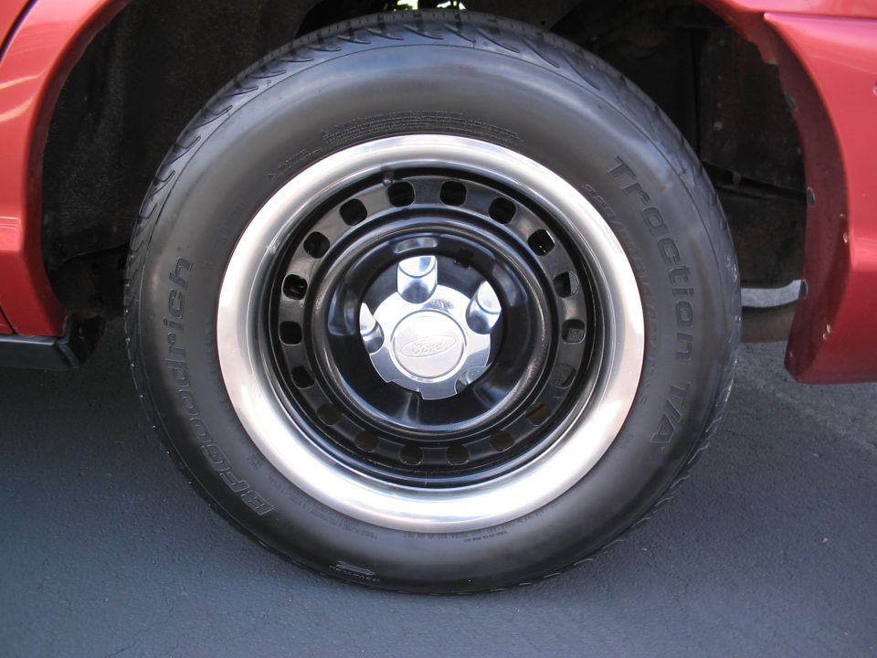 Red car's front wheel with a BFGoodrich Traction T/A tire on a black steel rim with a chrome Ford hubcap