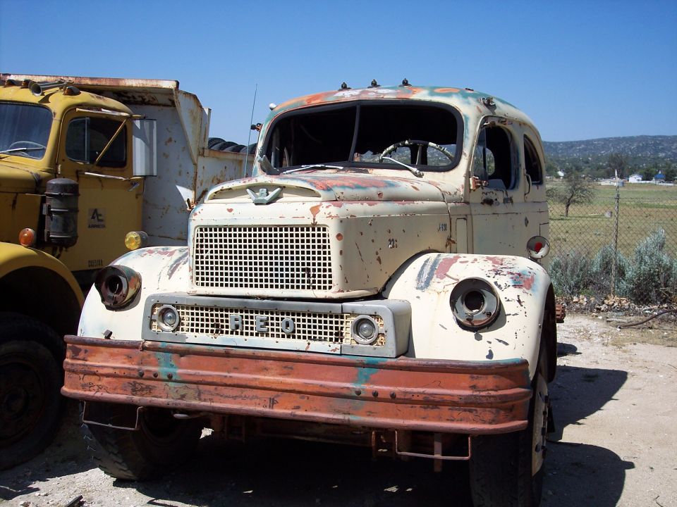 Front view of a weathered truck with a prominent grille and rust. Another truck is partially visible to the left