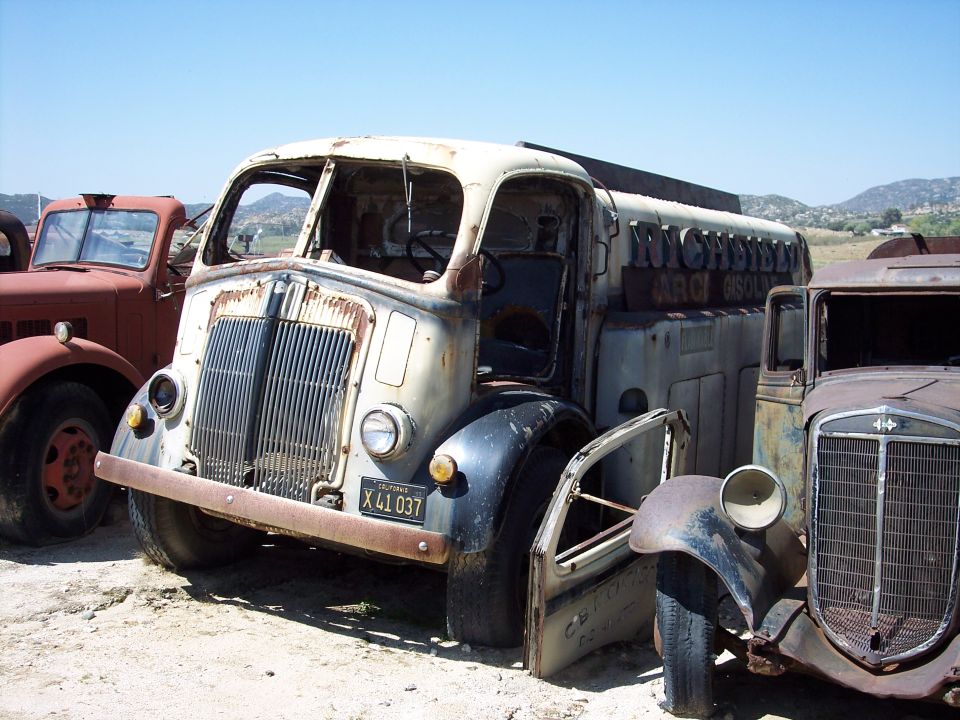 rusted Richfield gasoline truck with doors open, parked next to other old trucks