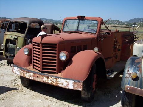 1981 Kenworth W900A - A rusty red fire truck sits in a junkyard with other vehicles.