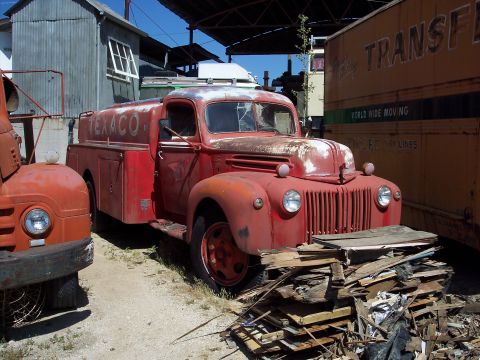 1981 Kenworth W900A - A vintage red Texaco tanker truck sits parked next to other vehicles and structures.