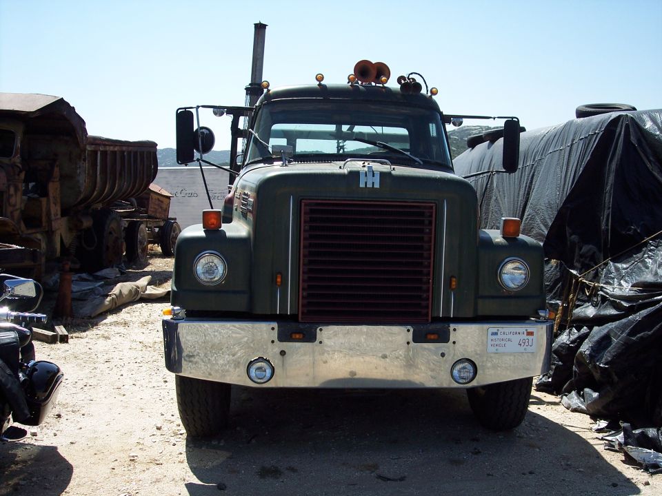 Front view of an International truck with a chrome bumper and a dark grille. Other vehicles and tarps are visible in the background