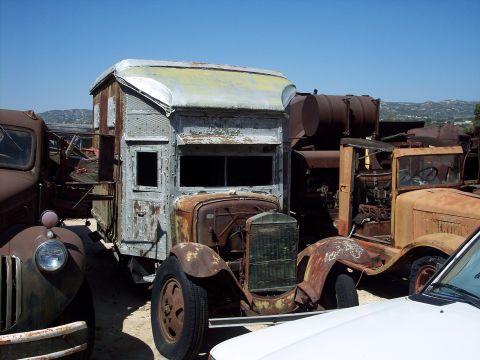 1981 Kenworth W900A - A collection of old trucks and vehicle parts are seen in a junkyard under a clear blue sky.