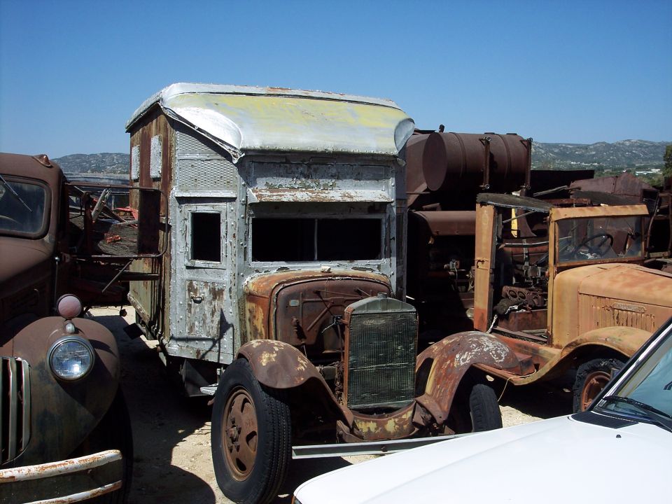 Rusty truck cab with a boxy sleeper and exposed engine, parked in a junkyard
