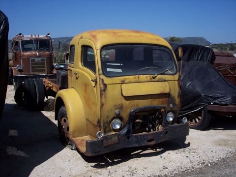 1981 Kenworth W900A - Weathered yellow truck cab sits in a yard with another truck in the background.