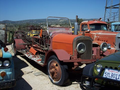1981 Kenworth W900A - Multiple old trucks are parked in a junkyard under a clear blue sky.