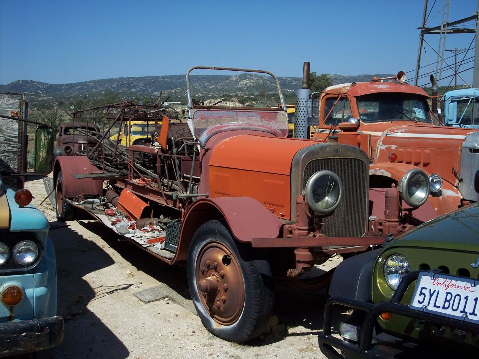 Front view of a rusty, old fire truck with other vehicles in the background