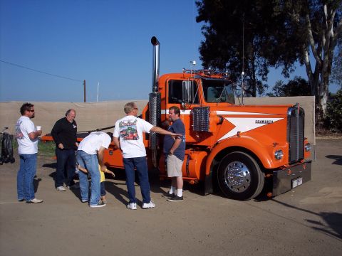 1981 Kenworth W900A - A group of men gather around a bright orange 1981 Kenworth W900A semi-truck on a sunny day.