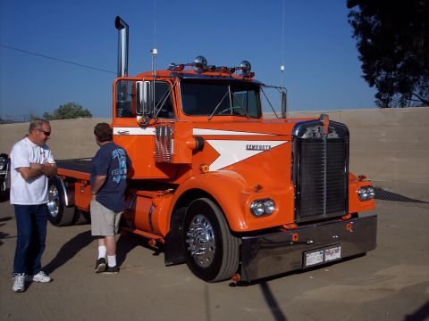 1981 Kenworth W900A - A bright orange 1981 Kenworth W900A semi-truck is parked outdoors with two men standing nearby.
