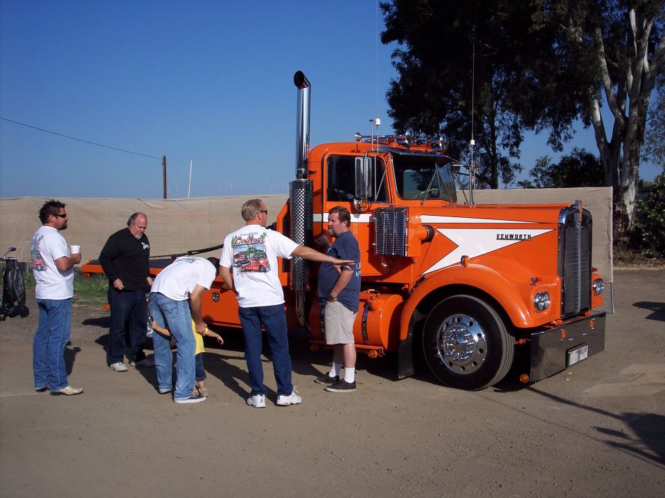 Orange Kenworth truck with chrome stack, people gathered around at outdoor show