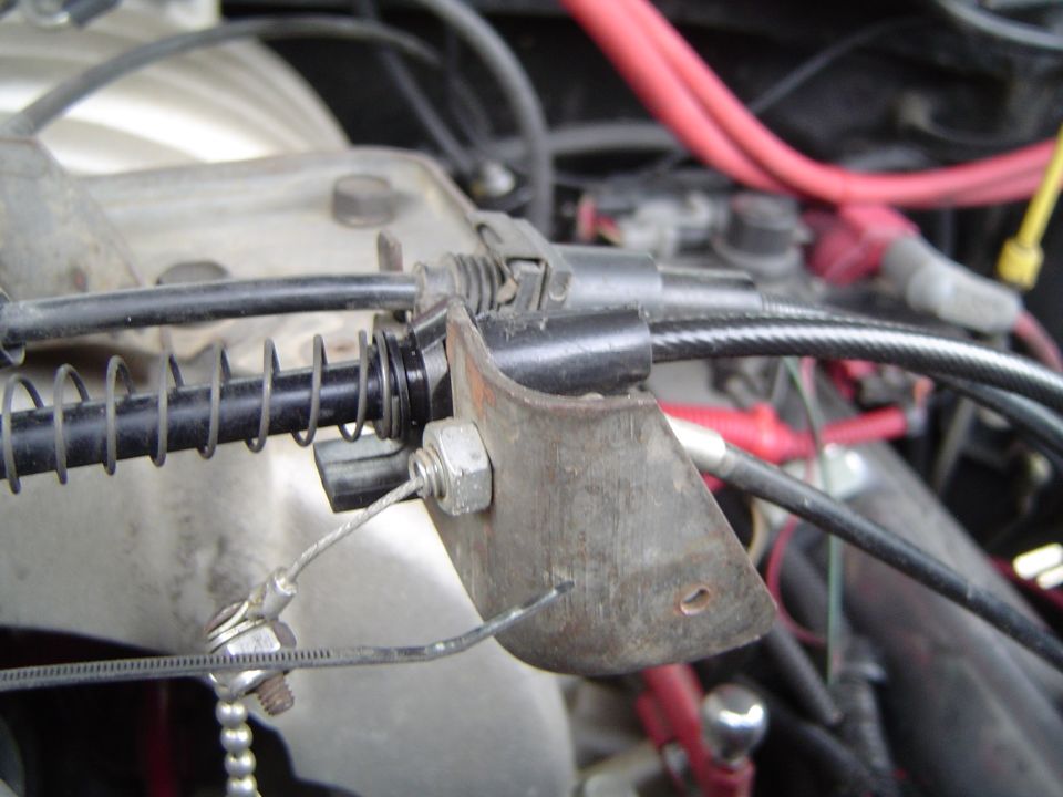 Throttle cable bracket with return spring and red spark plug wires on engine
