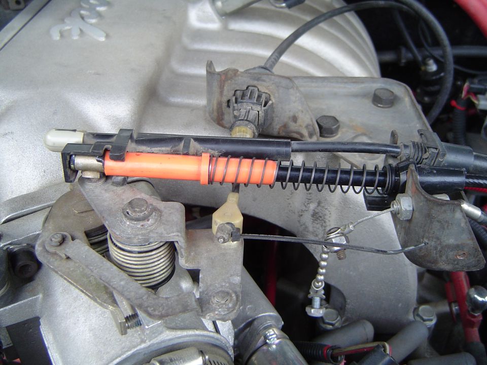 Throttle linkage with orange rod, coil springs and cables on an engine