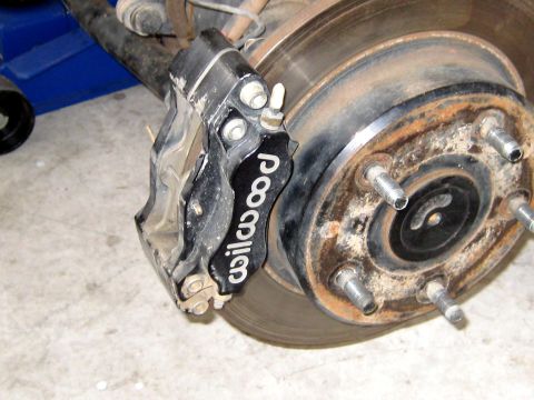 1996 Ford Bronco - Close-up of a black Wilwood brake caliper mounted on a rusty rotor and hub assembly.
