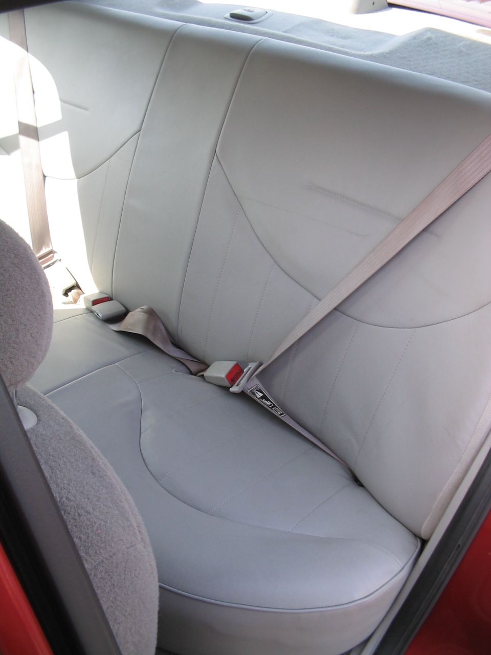 Light gray leather rear car seats with beige seatbelts and red buckles