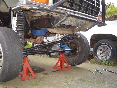 1978 Ford Bronco - The front suspension of a 1978 Ford Bronco is elevated on red jack stands, revealing custom modifications and a blue differential.