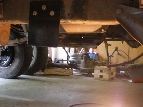 1993 Ford Bronco - The underside of a vehicle shows its rear axle, leaf springs, and differential, with wooden blocks providing support.
