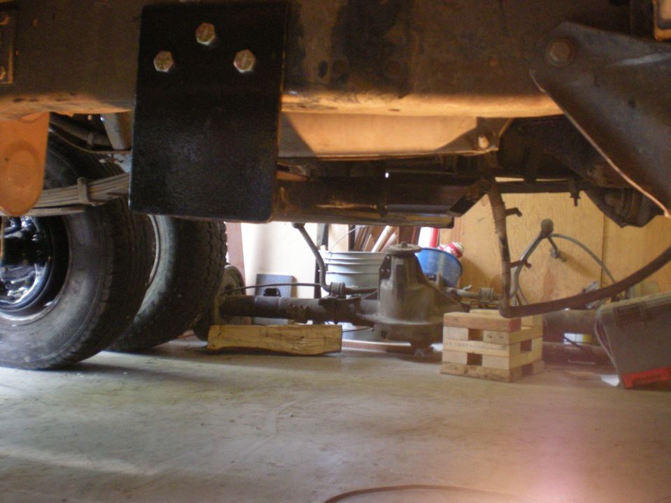 Underbody view of a vehicle's rear axle and leaf springs, supported by wooden blocks
