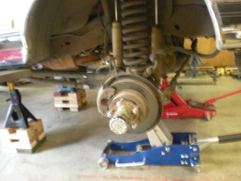 1993 Ford Bronco - Close-up view of a vehicle's front suspension and braking system, with various jacks and stands supporting the chassis.