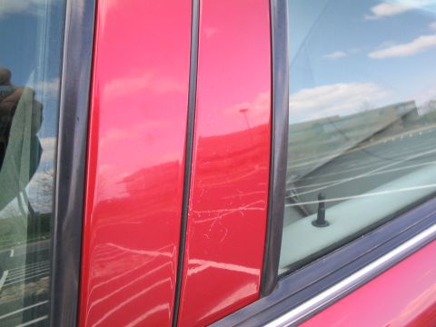 2001 Ford Crown Victoria - Close-up of a red car door showing scratches and reflections in the glass.
