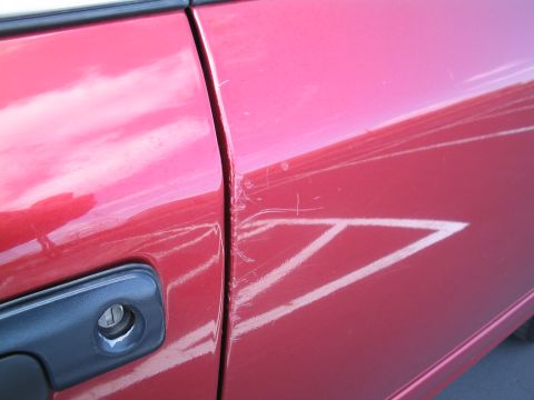2001 Ford Crown Victoria - Scratches are visible on the red paint of a car door next to the handle.