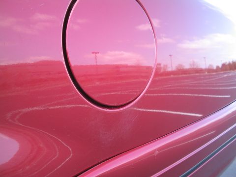 2001 Ford Crown Victoria - Close-up of a red car's side panel, revealing a gas cap and reflections of the surrounding environment.