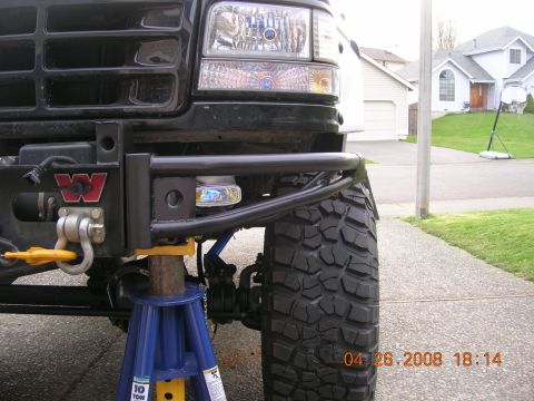 1996 Ford Bronco - Close-up of a modified Ford Bronco front end, supported by jack stands, with a large off-road tire visible.