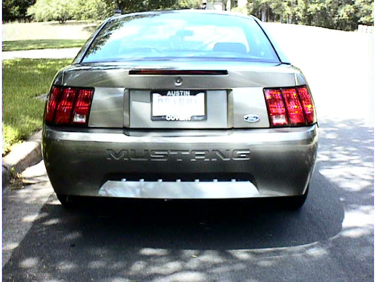 Rear of a gray Mustang coupe with Ford oval and Austin plate frame in dappled shade