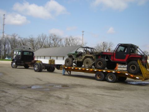 1992 Ford Bronco - A flatbed trailer carries two modified off-road vehicles, towed by a truck.