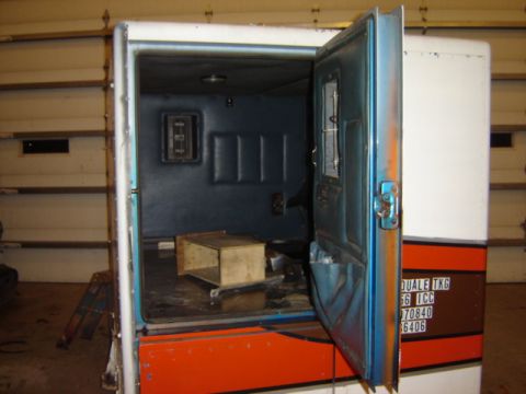 1992 Ford Bronco - The interior of a truck cab shows blue padded walls and an open door, with a wooden box on the floor.