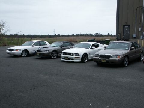 2001 Mercury Grand Marquis - A lineup of four cars, including two Ford Mustangs and two Mercury Grand Marquis, are parked outside a building.