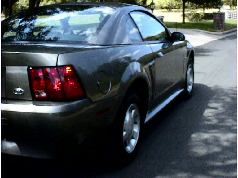 Rear three-quarter of a gray-gold Mustang coupe on a residential street