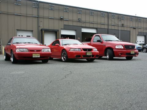 2001 Mercury Grand Marquis - Three red vehicles, including two Mustangs and a pickup truck, are lined up in front of a warehouse.