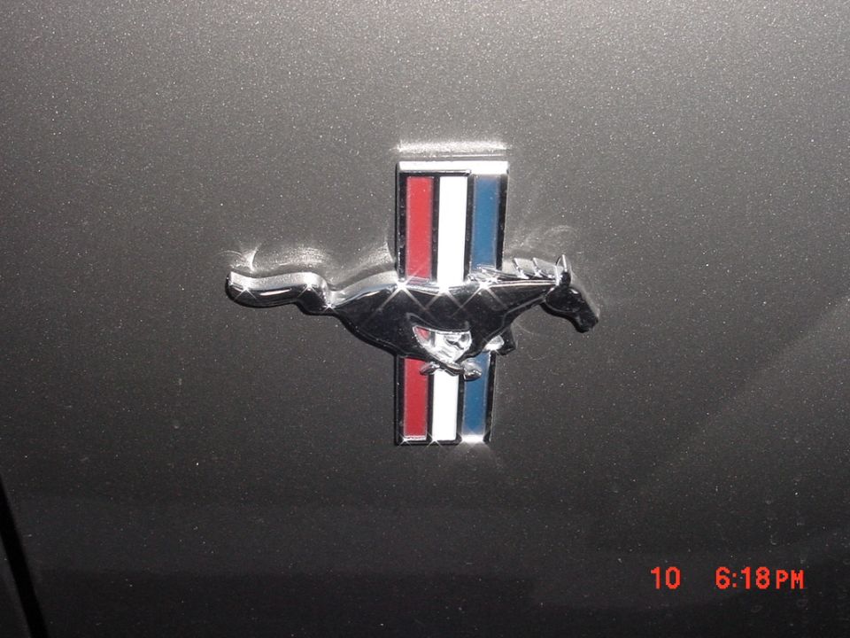 Chrome Ford Mustang emblem with red, white, and blue stripes on a dark gray car