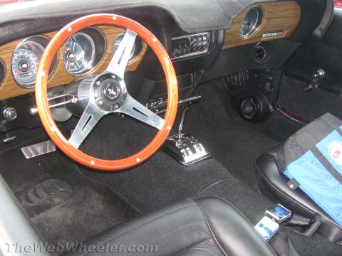 1968 Ford Mustang - The interior of a 1969 Ford Mustang Mach 1 features a wood-grain dashboard, an aftermarket steering wheel, and a chrome floor shifter.
