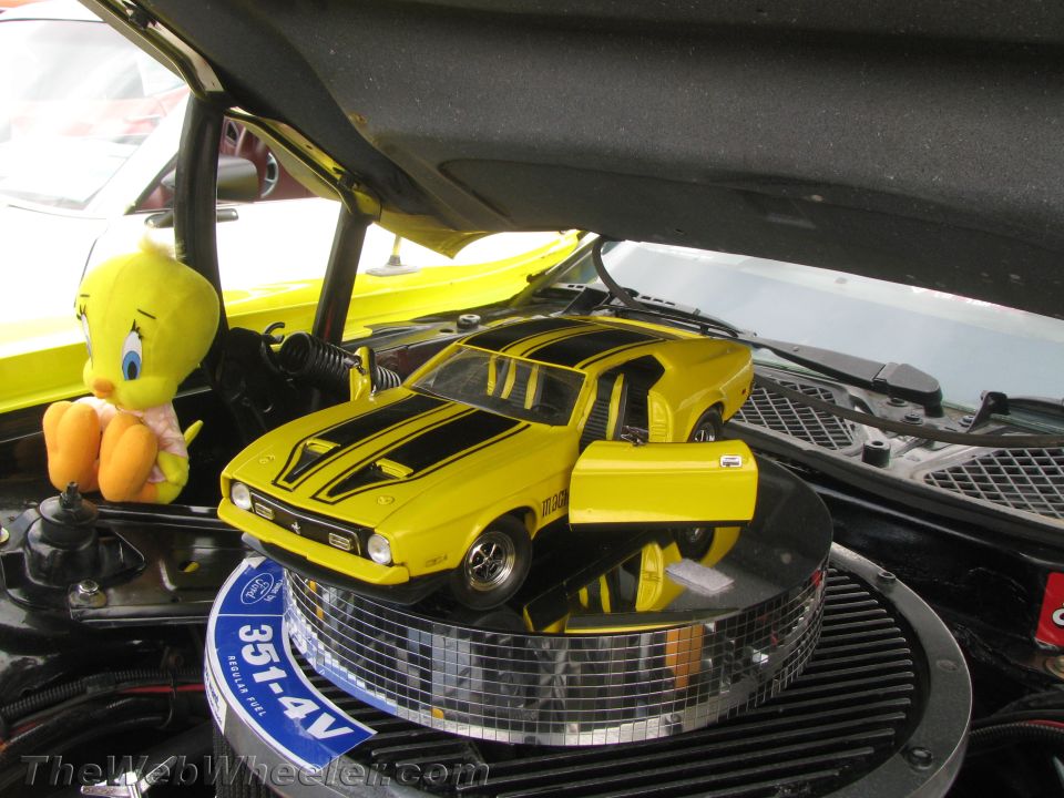 Yellow toy car with black stripes on a chrome base, next to a Tweety Bird plush toy, inside an engine bay
