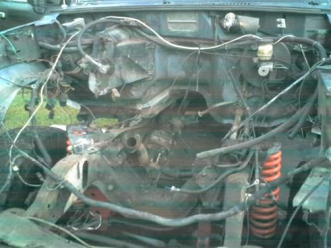 1995 Ford Bronco - The engine bay of a vehicle is shown with many wires and rusty parts, indicating disrepair.