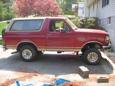 1995 Ford Bronco - This red Ford Bronco with a tan top is viewed from the side, showing its spare tire mounted on the rear door.