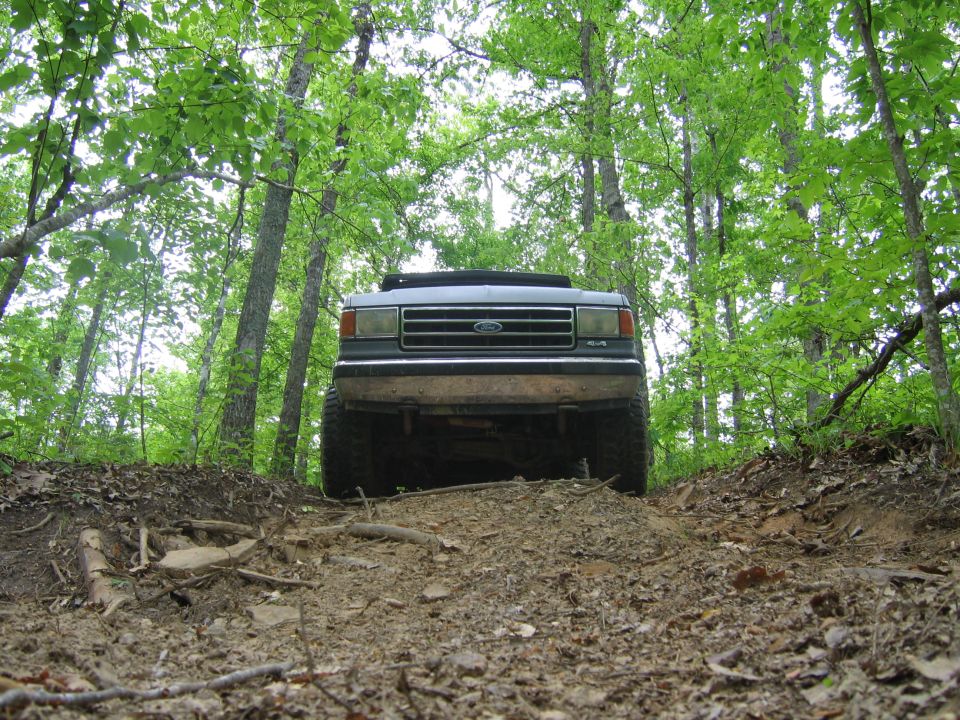 1989 Ford Bronco driving up a dirt path in a forest.