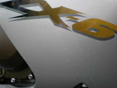 2002 Buell Lightning w/Fairing - A close-up view of the 'XB' graphic on a silver motorcycle fairing shows numerous surface scratches.