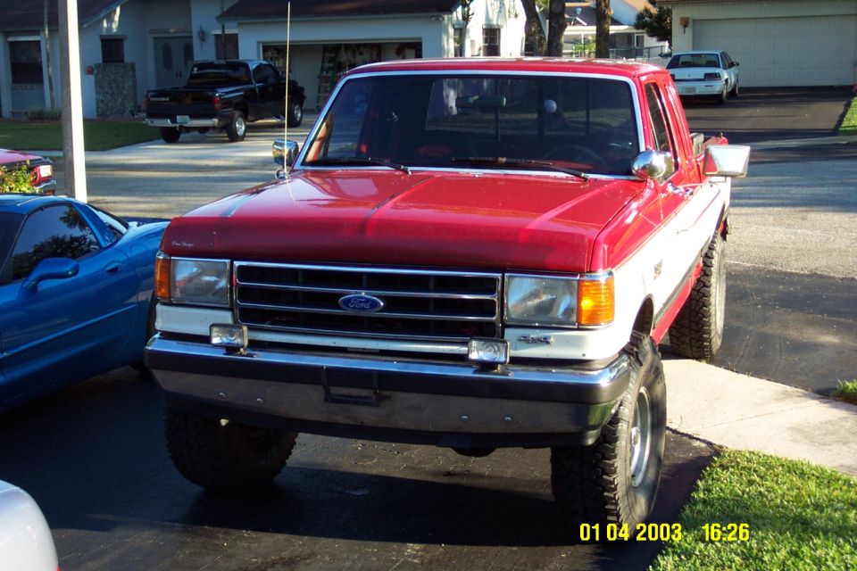 Front view of a red and white 1989 Ford F-150 pickup truck parked next to a blue sports car